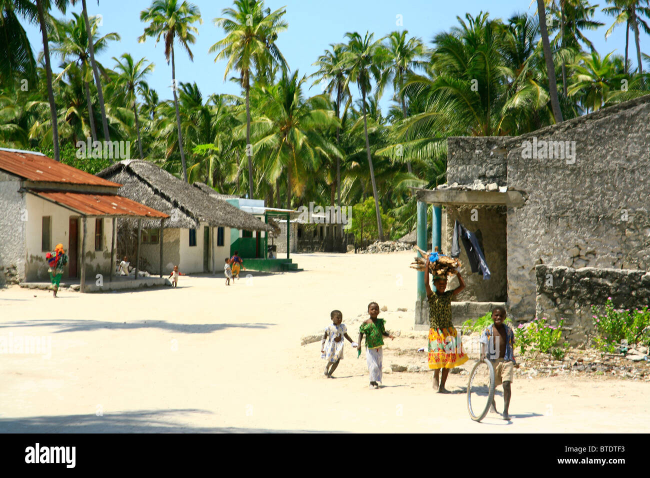 Woman carrying firewood and young children walking in a village on Ibo Island Stock Photo