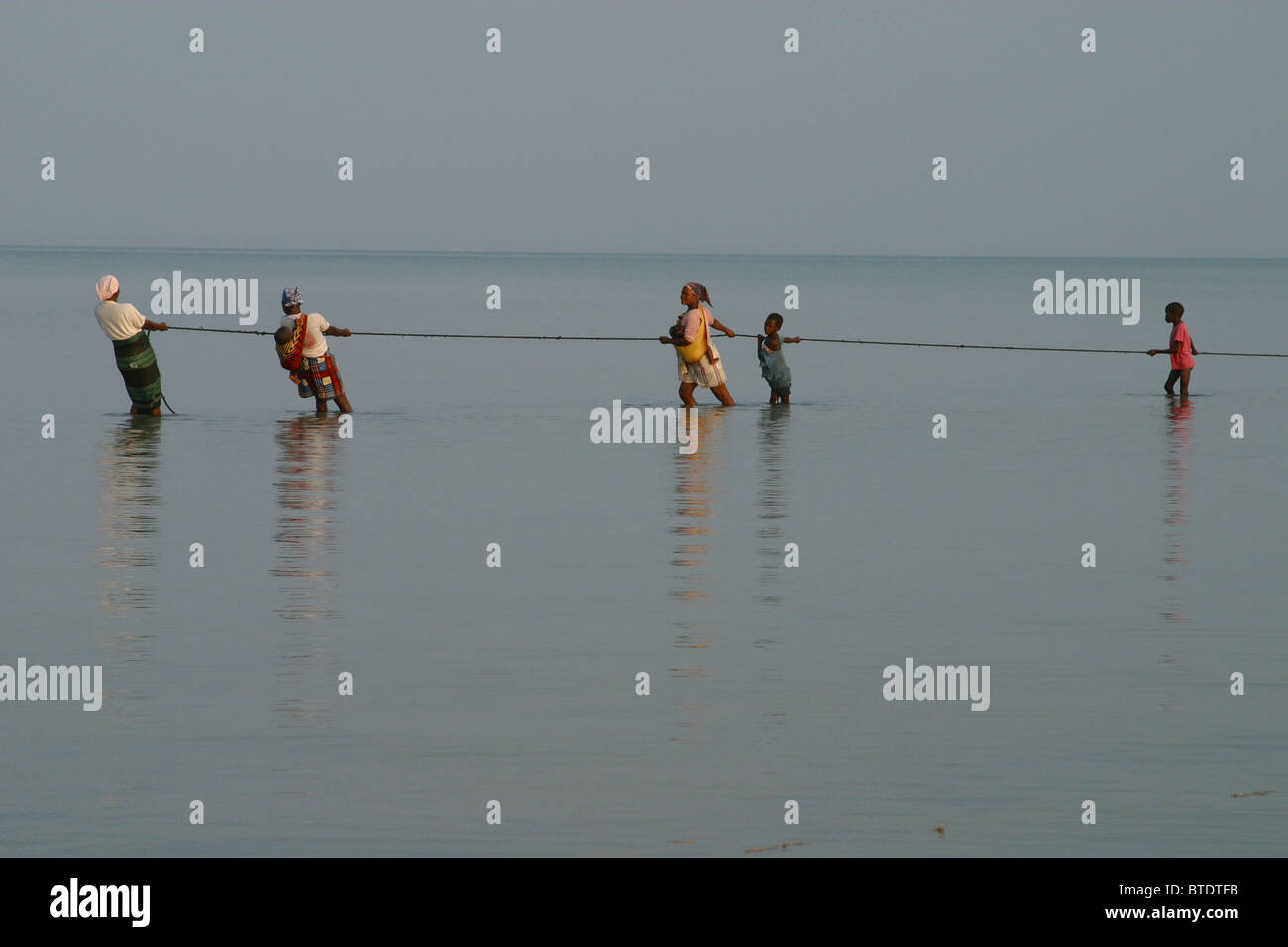 Women and children pulling on a rope to help bring in fishing nets Stock Photo