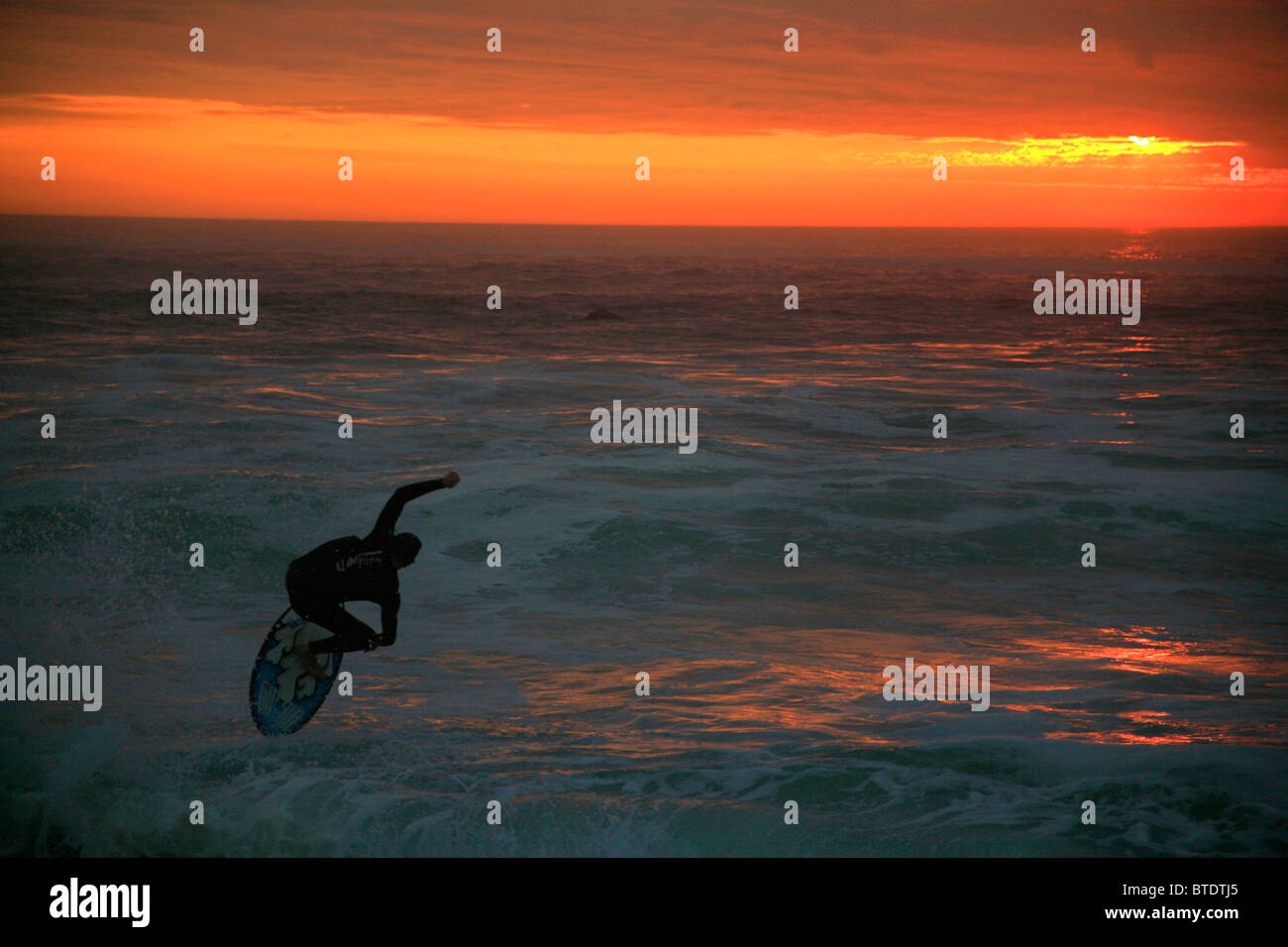 Surfer catching a wave at sunset Stock Photo