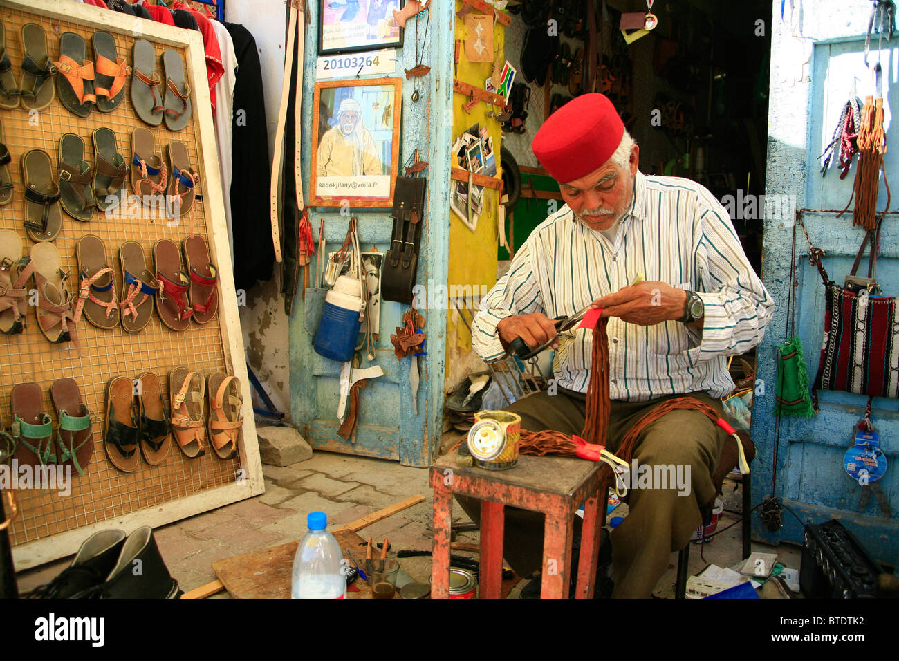Shoe repair man sitting at the entrance of a shop cutting strips of