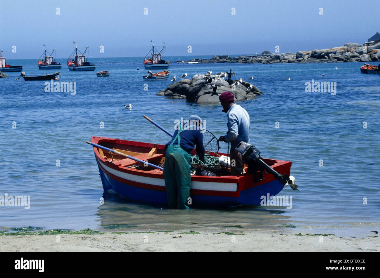 Two fishermen load their crayfish trap onto their skiff at Jacobs Baai Stock Photo