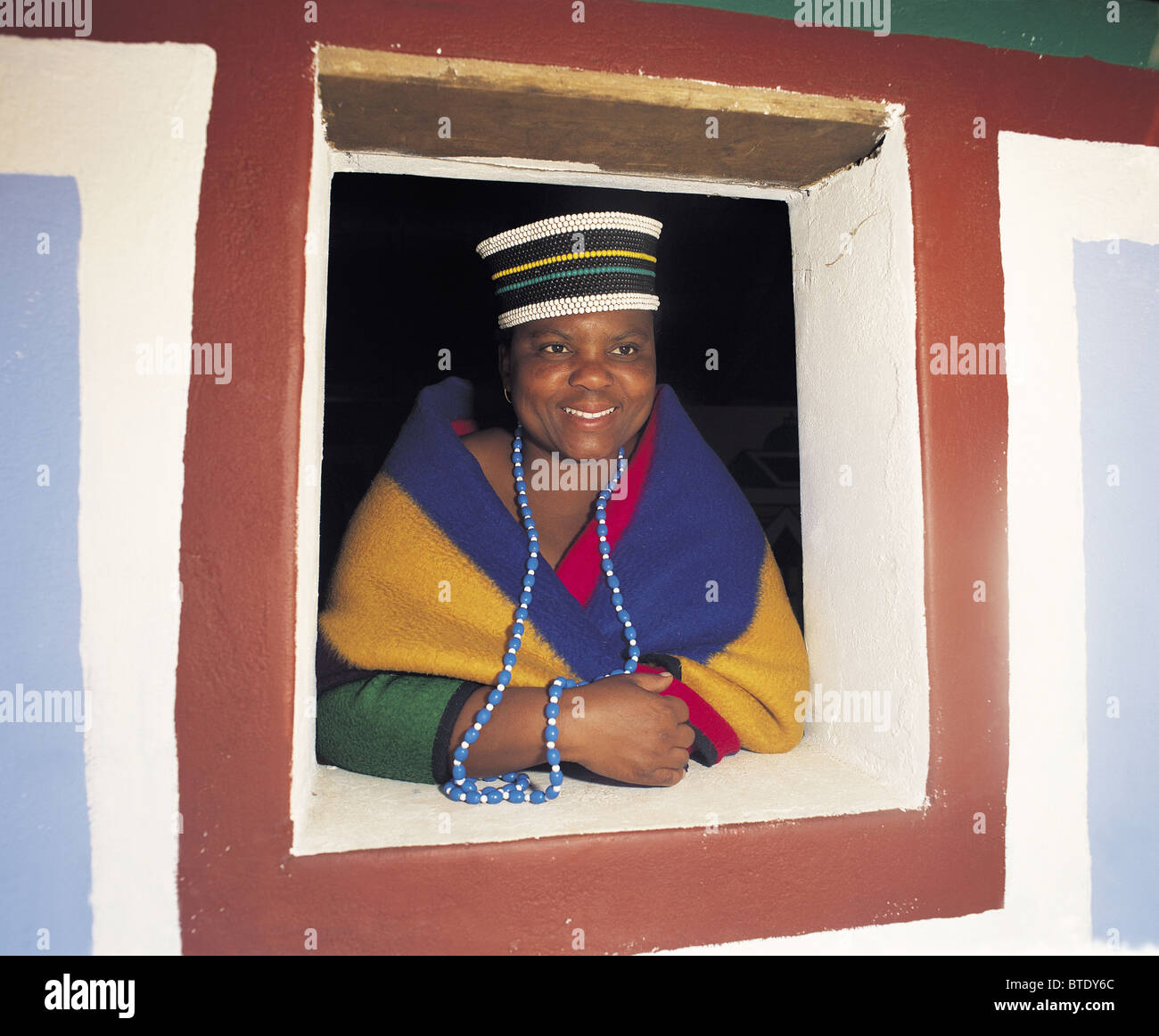 A portrait of a smiling Ndebele woman looking out of a window. Stock Photo