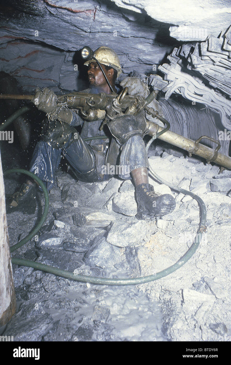 Drilling in an underground gold mine showing high pressure hoses and cramped working conditions. Stock Photo