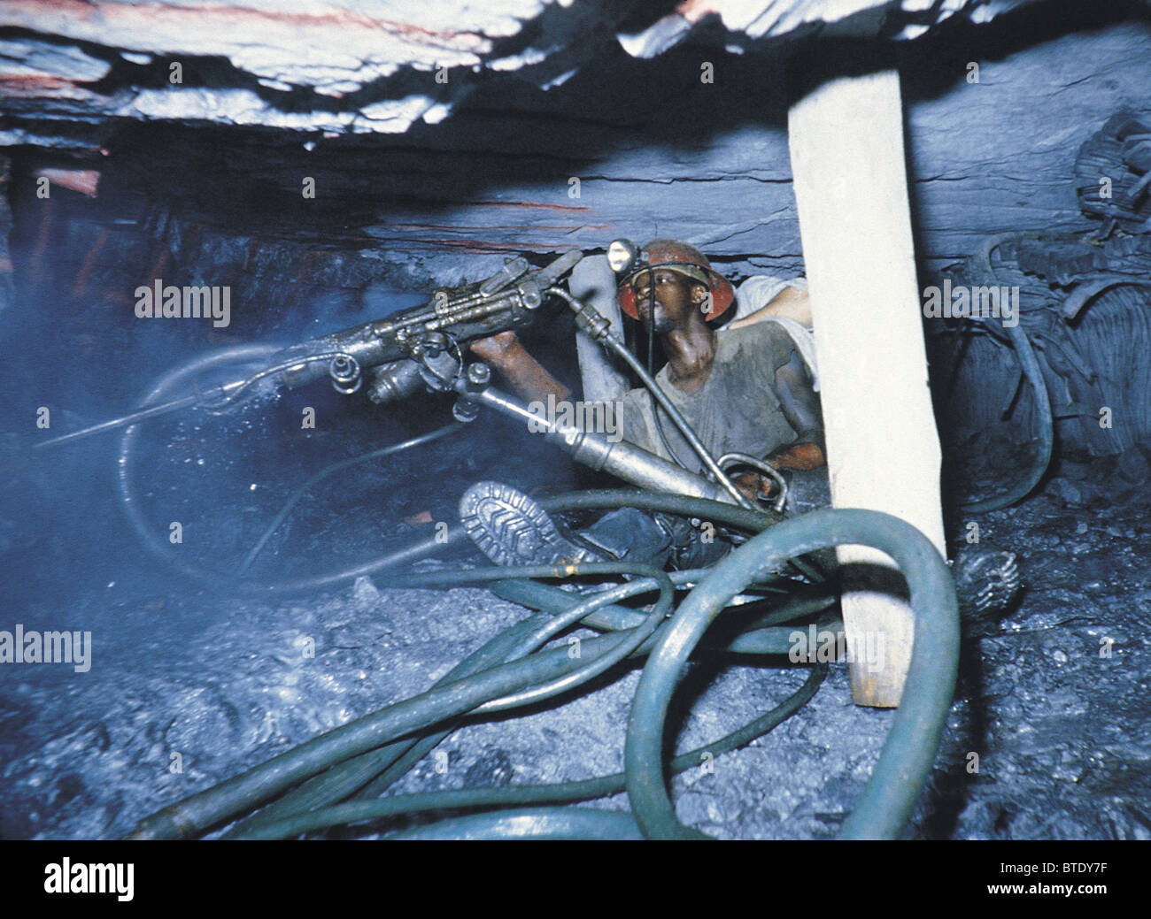Drilling underground in a gold mine showing high pressure hoses and cramped working conditions. Stock Photo