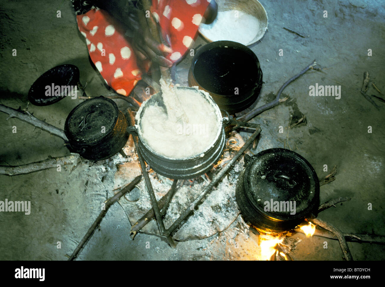 Woman preparing maize meal porridge in cast iron cooking pot over the