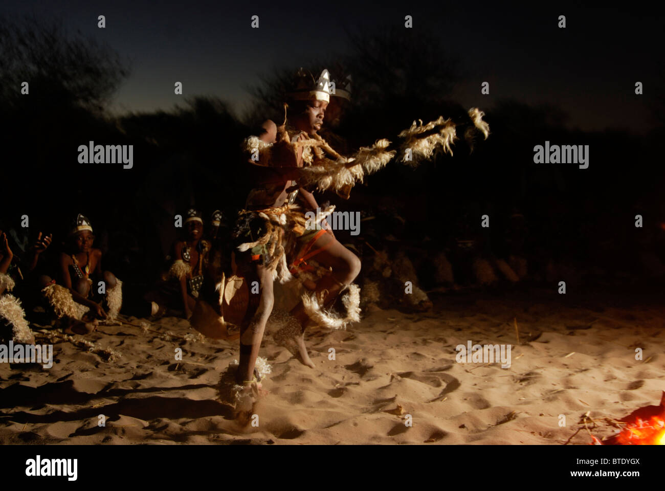 Young Zulu boy dancing around the fire in front of a row of seated boys Stock Photo