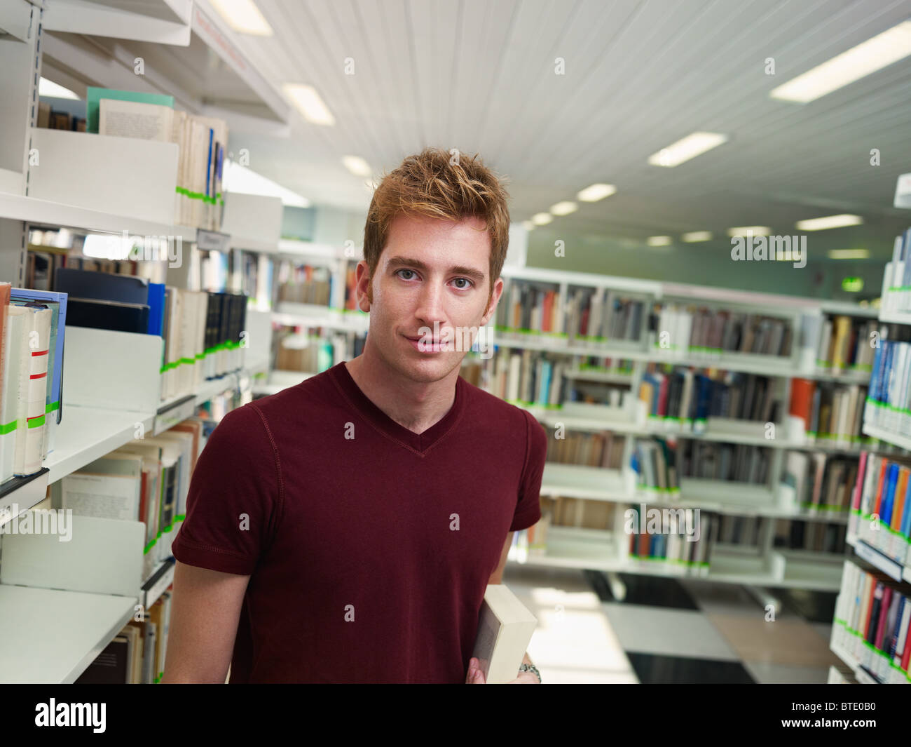 male college student with book standing near shelf in library ...