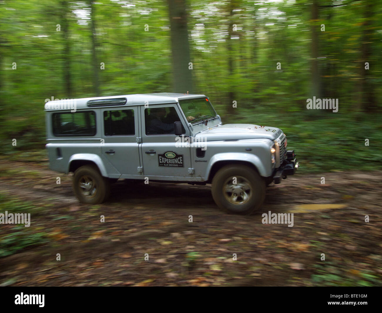 Silver Land Rover Defender driving through a forest at the Domaine d'Arthey estate in Belgium Stock Photo