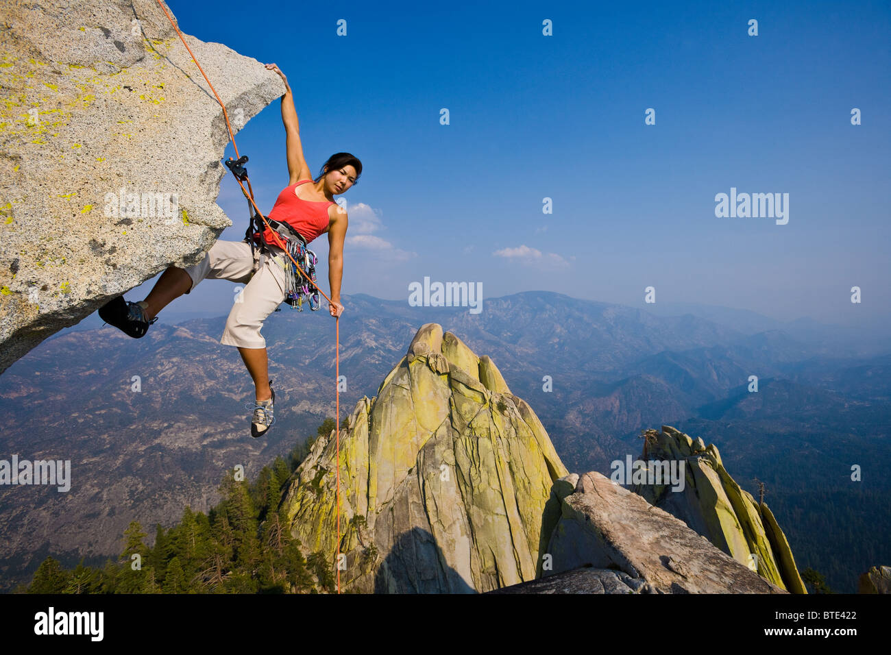 Female climber rappelling from the summit of an overhanging cliff Stock