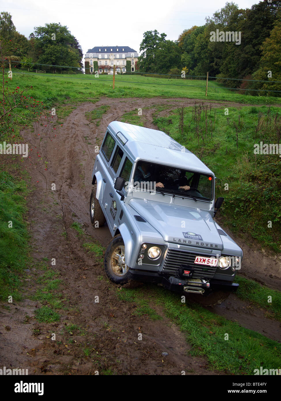 Silver Land Rover Defender driving down a very steep and very slippery slope at Domaine d'Arthey estate, Belgium Stock Photo