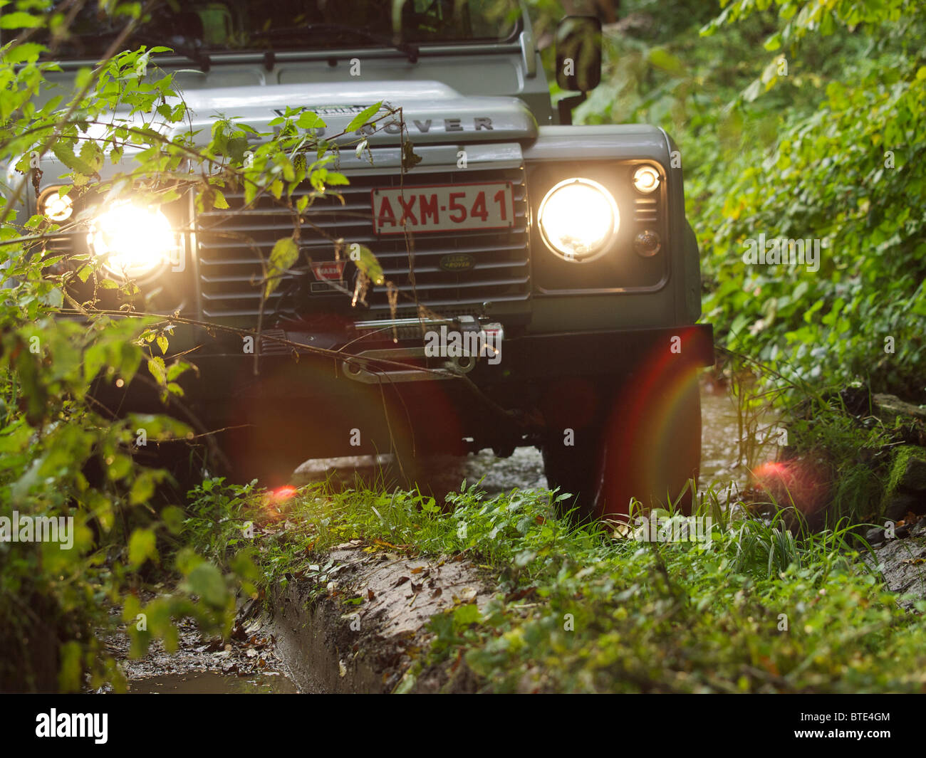 Silver Land Rover Defender driving through a very muddy path at the Domaine d'Arthey estate in Belgium Stock Photo