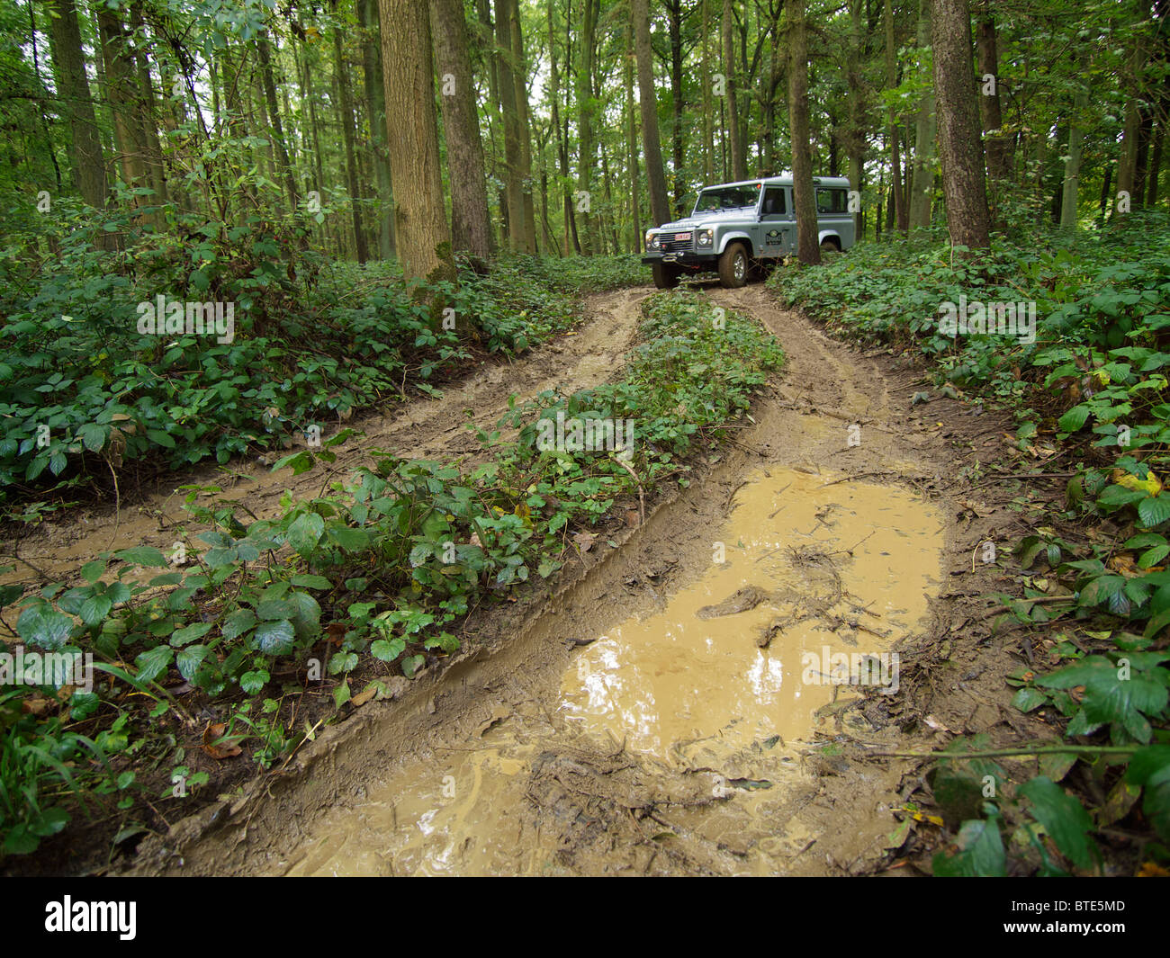 Silver Land Rover Defender driving on an extremely muddy path at the Domaine d'Arthey estate in Belgium Stock Photo