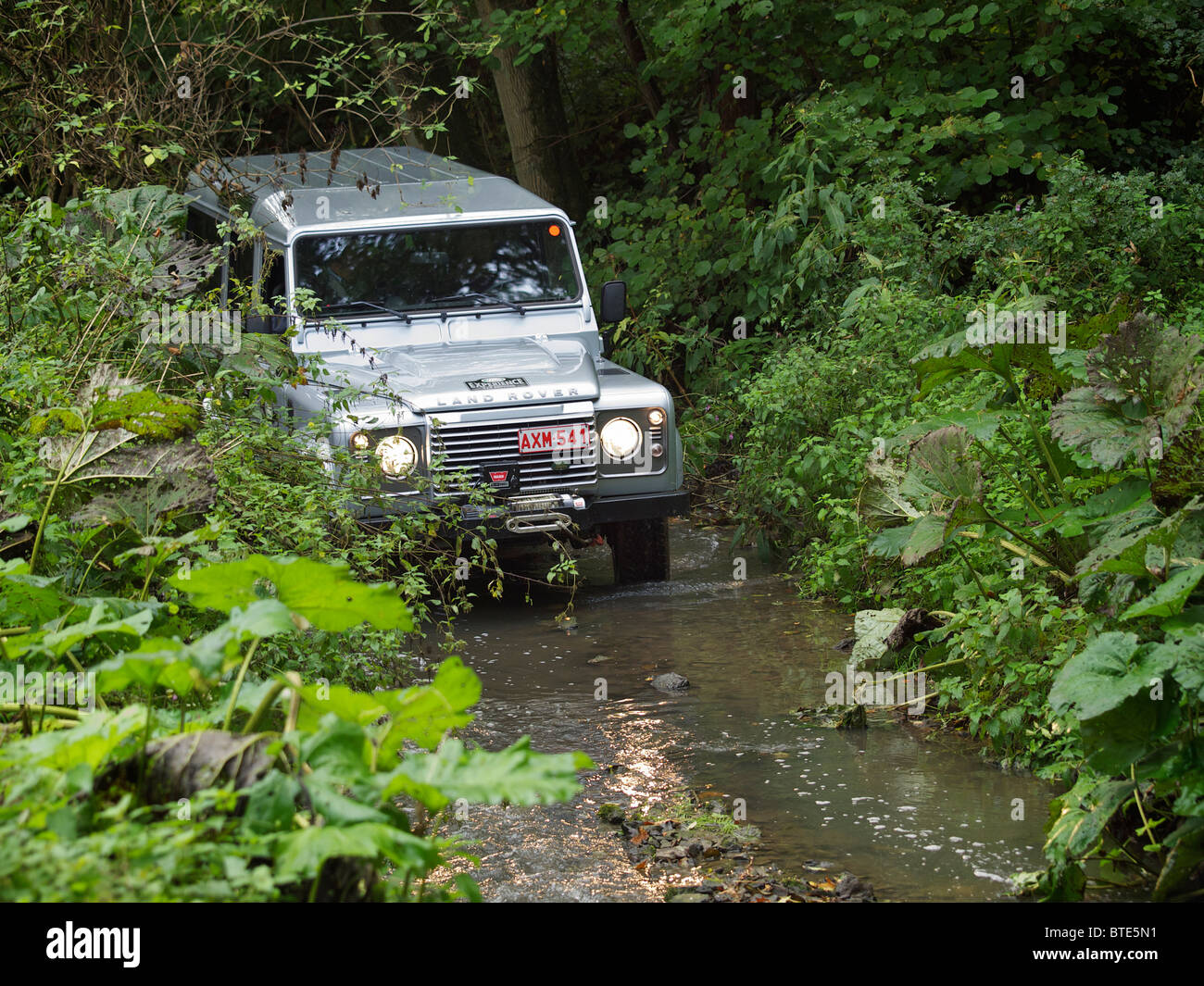 Silver Land Rover Defender driving through a creek at the Domaine d'Arthey estate in Belgium Stock Photo