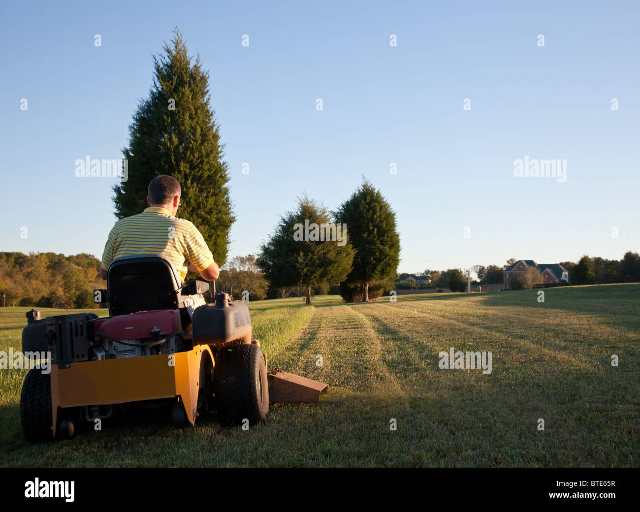 Middle aged man on zero turn mower cutting grass on a sunny day with the sun low in the sky Stock Photo