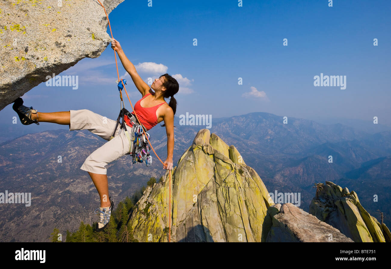 Female climber rappelling from the summit of an overhanging cliff Stock