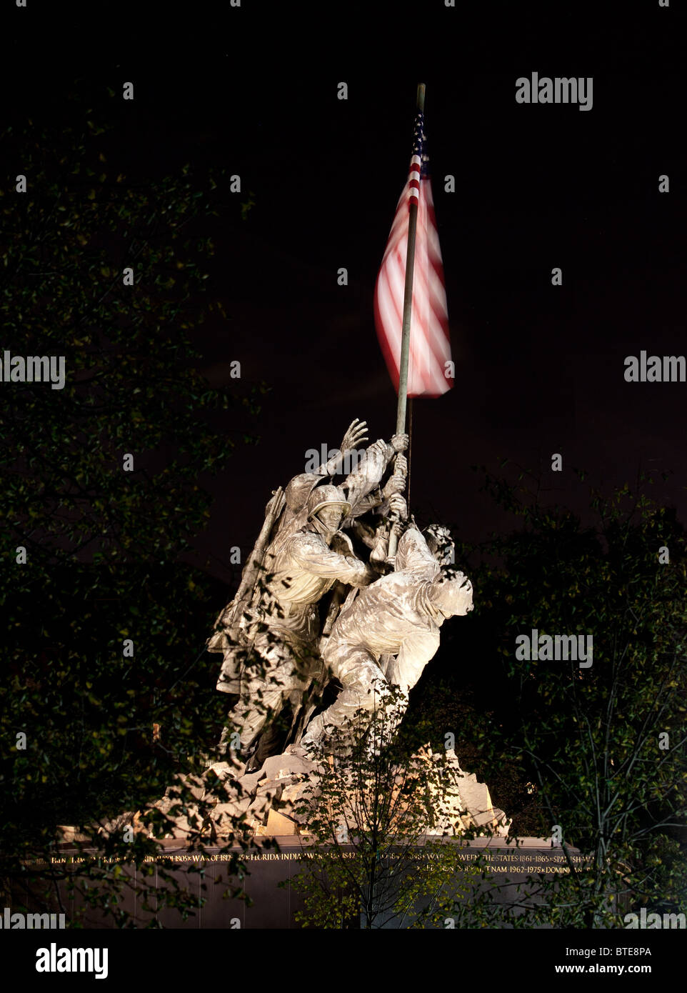 Statue commemorating Iwo Jima at night lit by floodlights and seen through the trees and branches Stock Photo