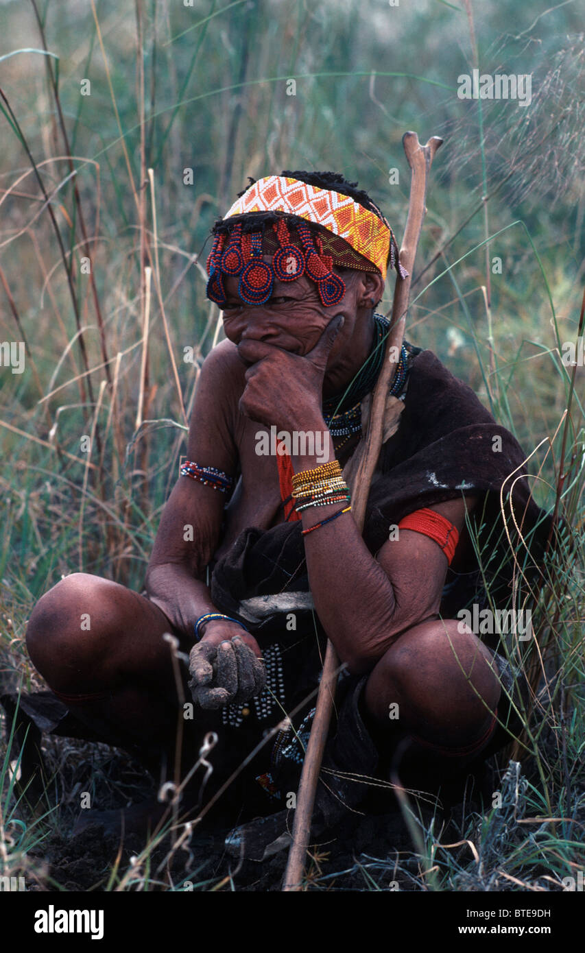 An elderly Kung Bushman woman sitting on her haunches with her root digging stick Stock Photo