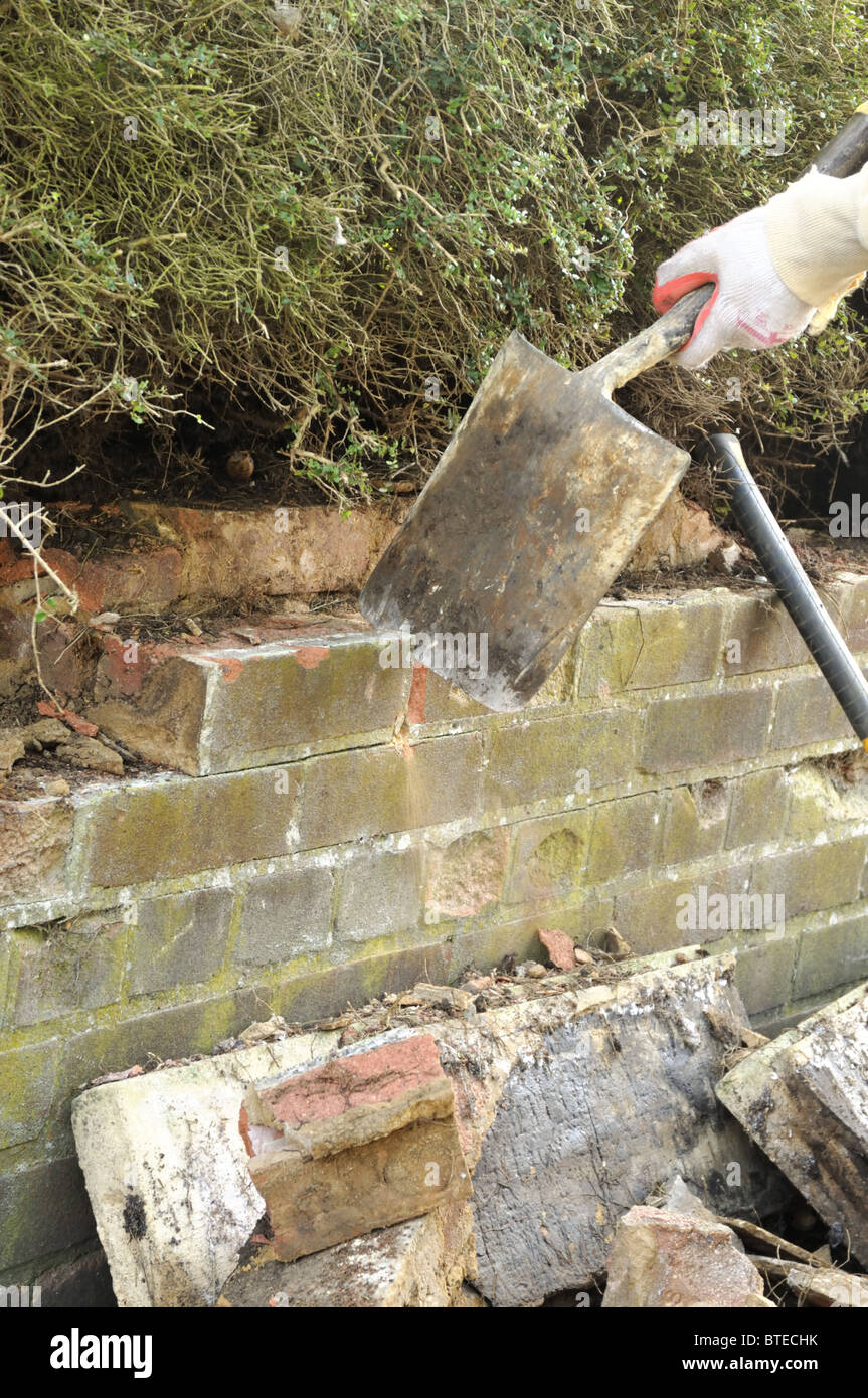Knocking down old brick garden wall with shovel Stock Photo Alamy