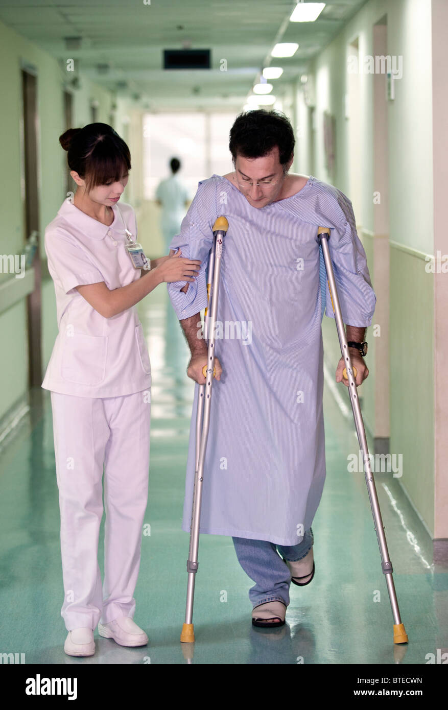 Nurse helping patient walk down hospital corridor on crutches Stock Photo Alamy