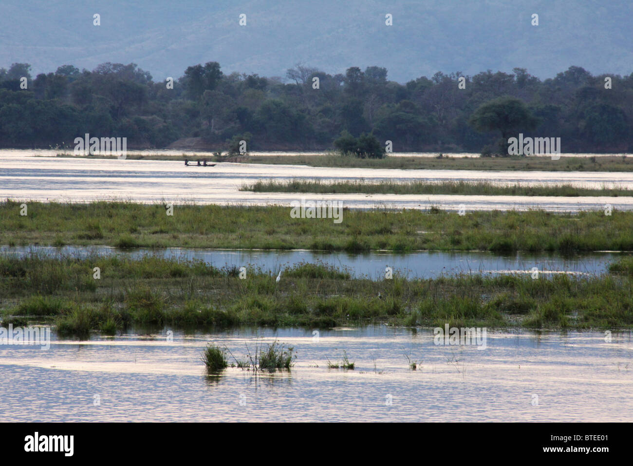 Zambezi river stretching over a vast area with trees in the background and small dugout canoe in the distance Stock Photo
