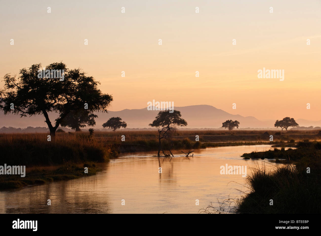 Sunset with Zambezi River in the foreground and the mountain and trees in the background Stock Photo