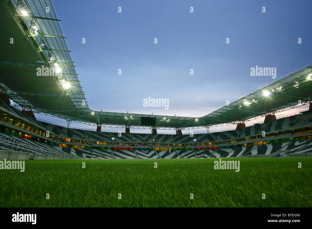 Interior of the Mbombela stadium at dusk showing the zebra-striped seating an a lush, green, playing surface Stock Photo
