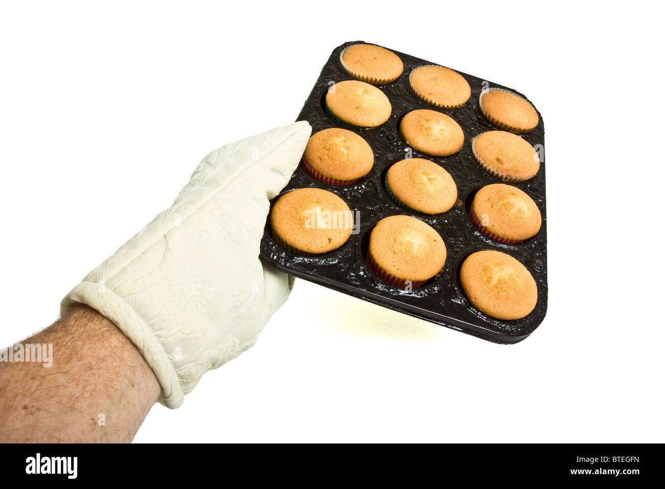 Hand wearing oven mitt holding hot tray of freshly cooked cup cakes. Stock Photo
