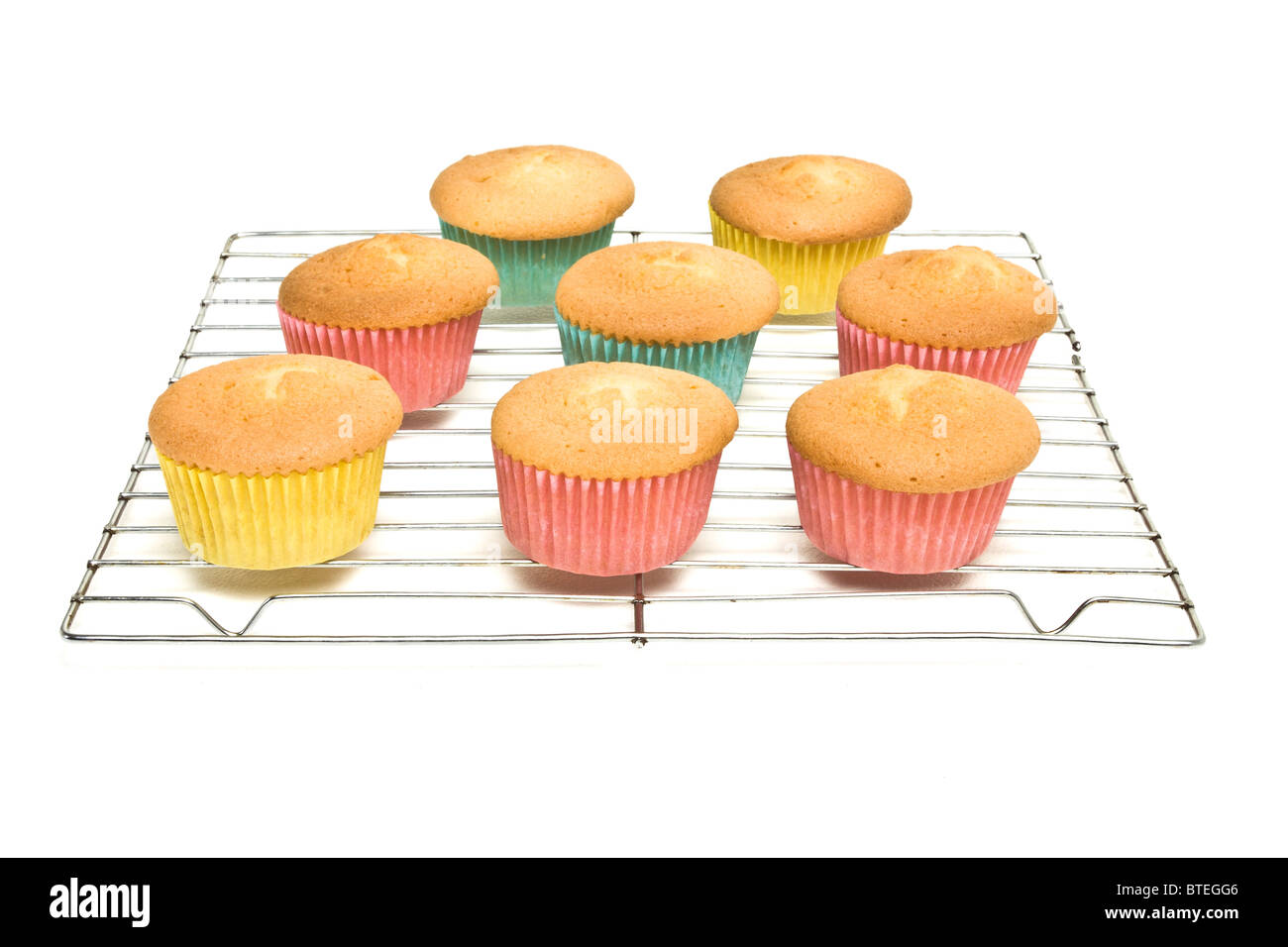 Home baked cupcakes cooling on wire mesh rack from low perspective isolated on white. Stock Photo