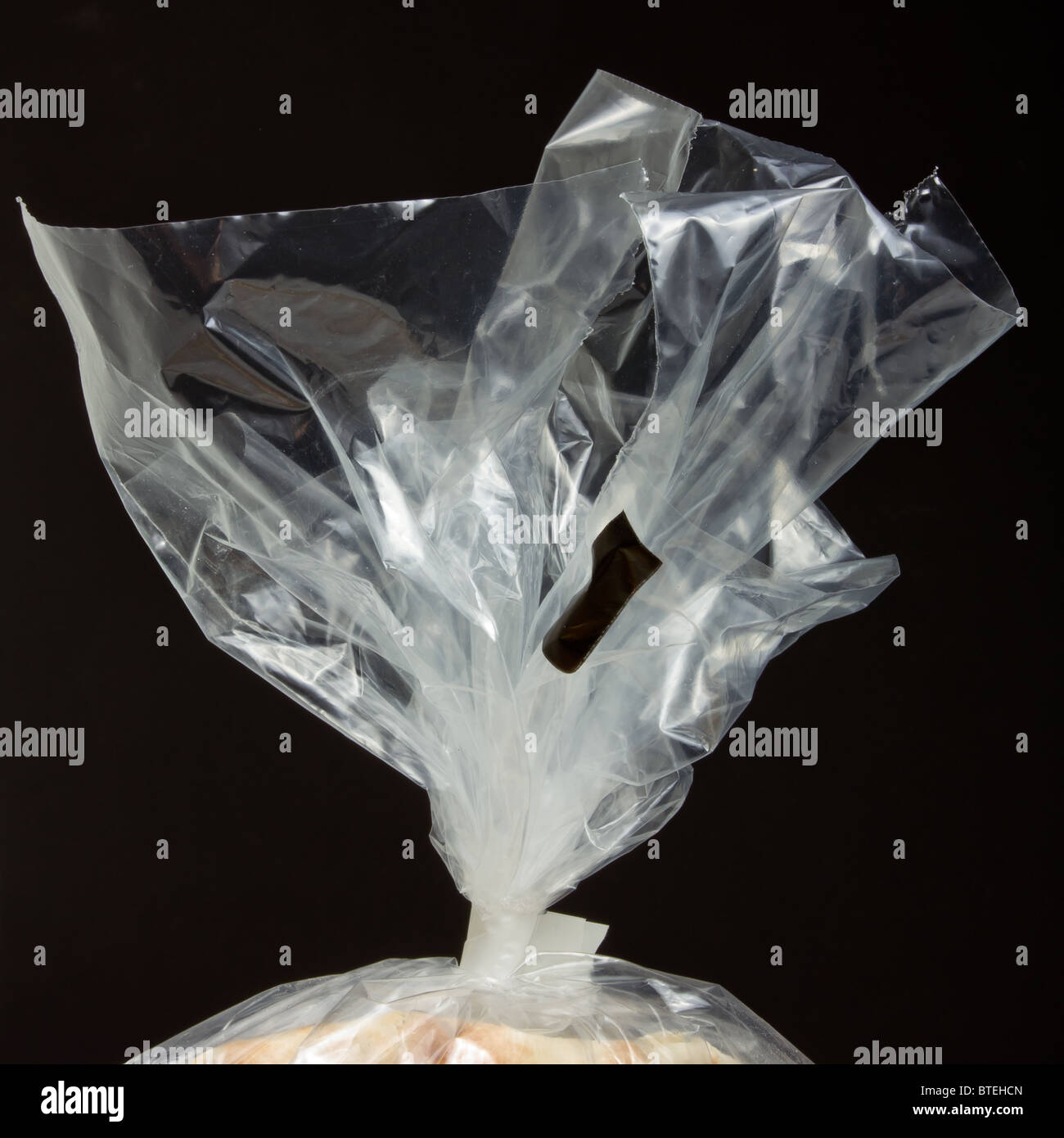 Neck of clear plastic food bag with tie against dark background. Stock Photo