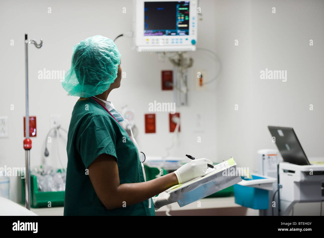 Nurse checking medical equipment monitor, recording data in medical