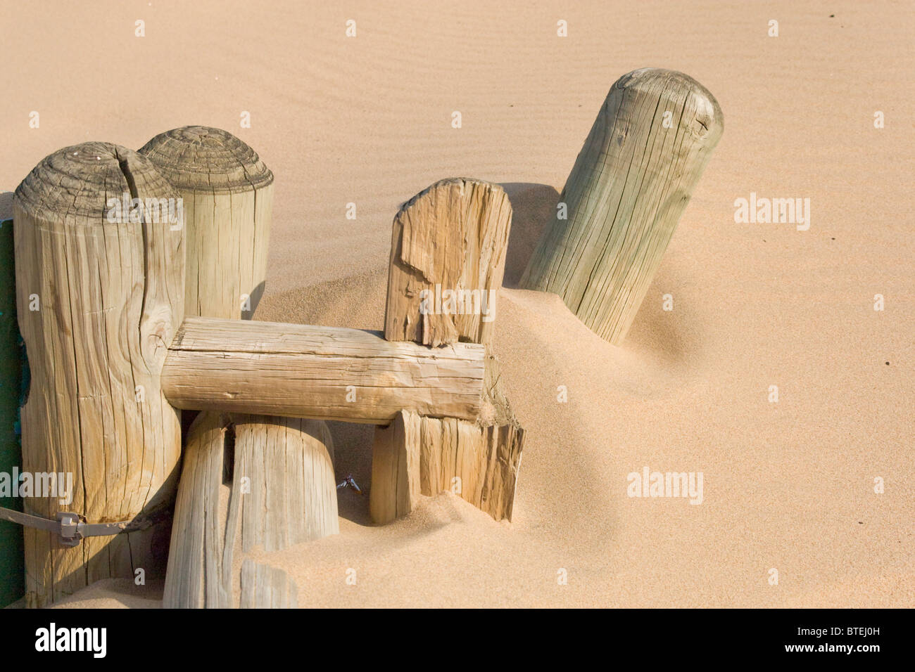 Old wooden fence poles half buried in beach sand Stock Photo