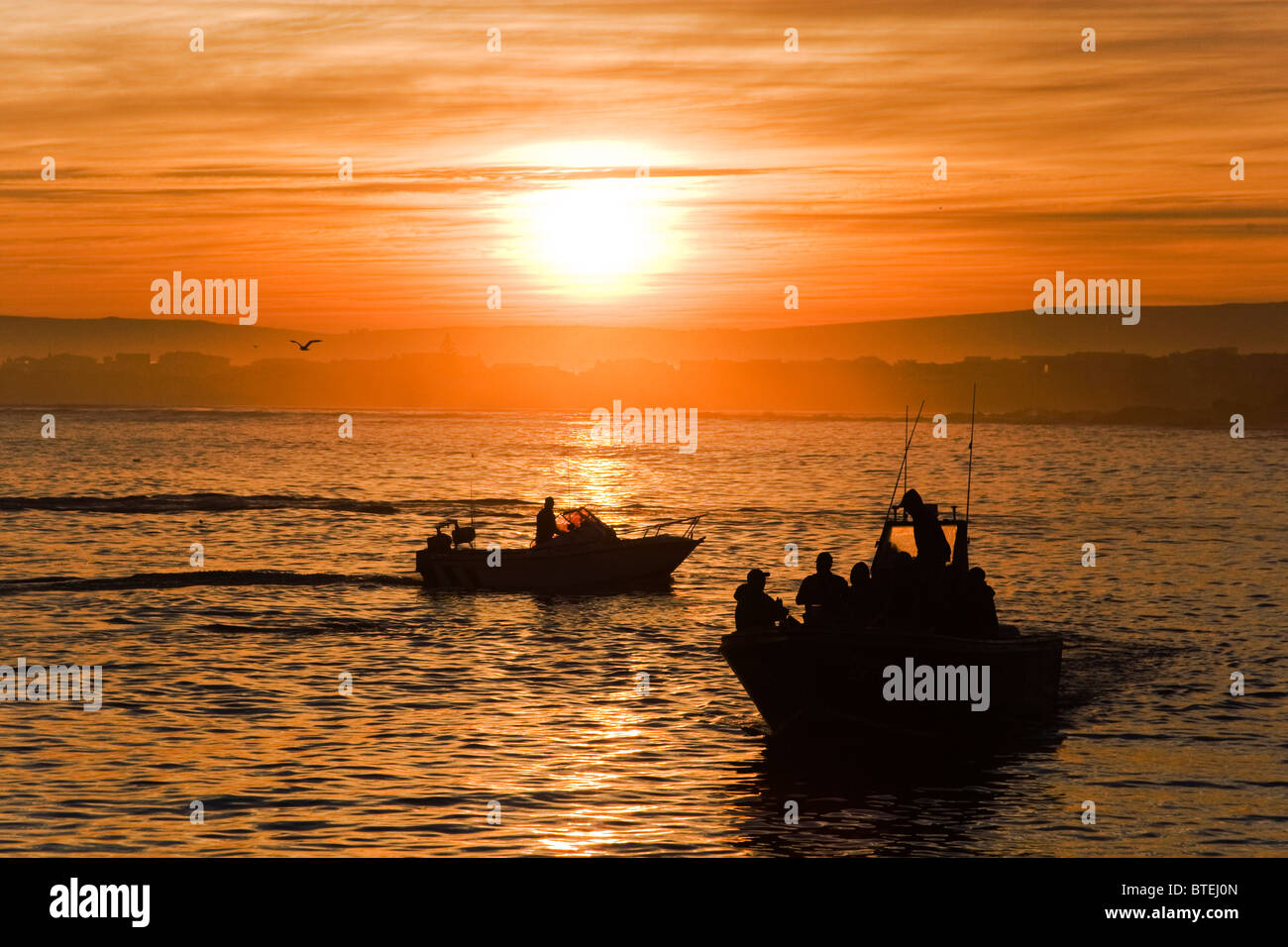 Fishing boat silhouetted in early morning sunrise and as it heads out to sea Stock Photo
