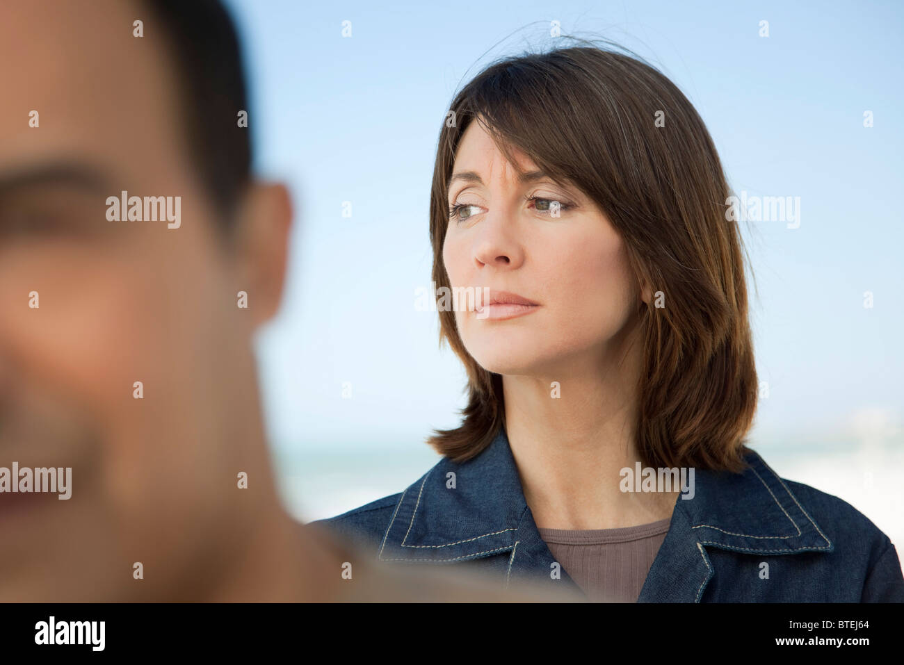 Woman looking away with furrowed brow, man in foreground Stock Photo