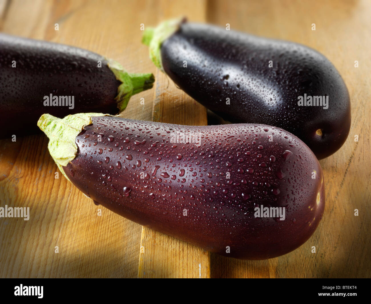 Fresh whole aubergines or eggplants with water droplets, uncut and un-cooked against a wood background Stock Photo