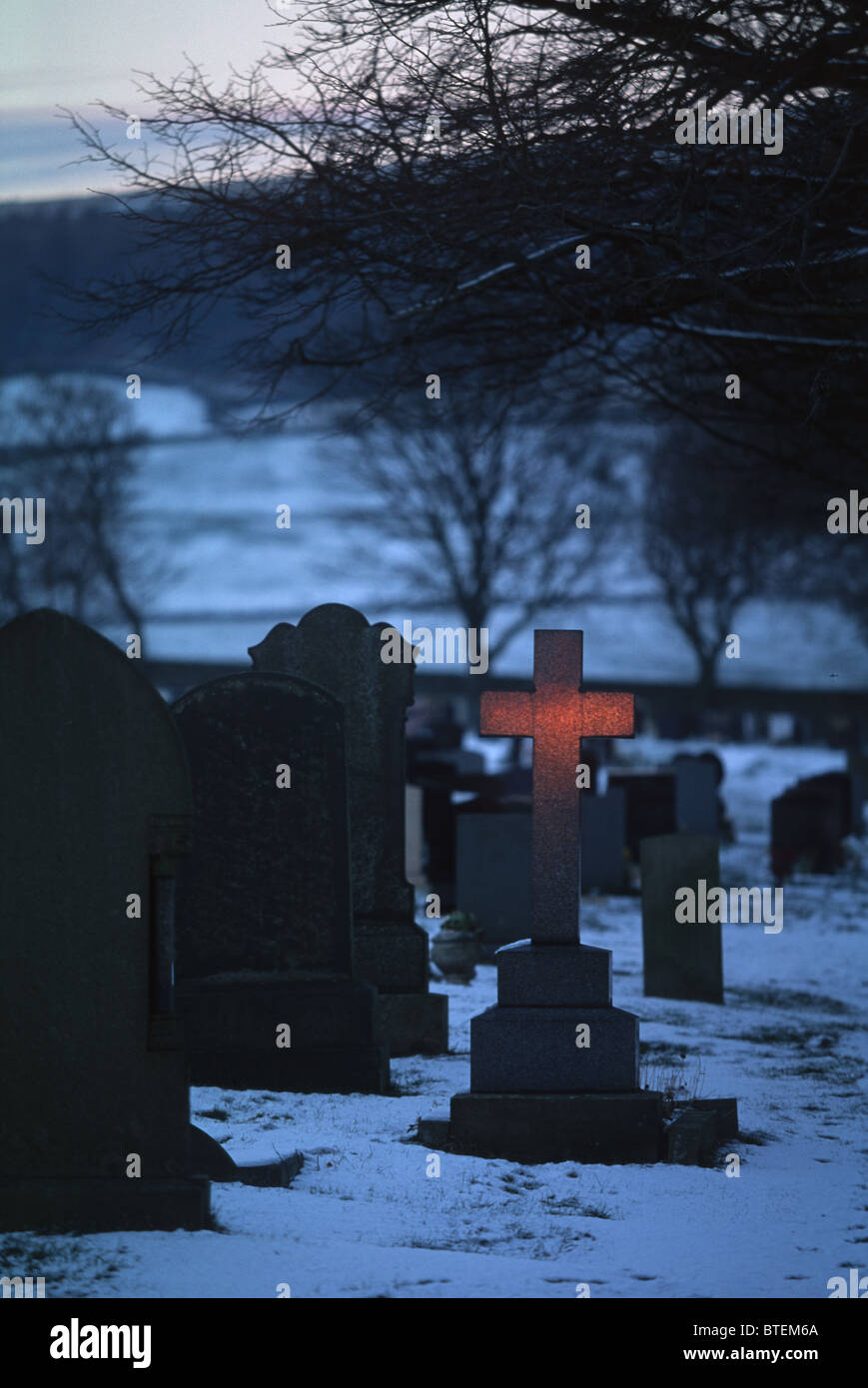 Last light at the graveyard and a marble grave cross lights up Stock