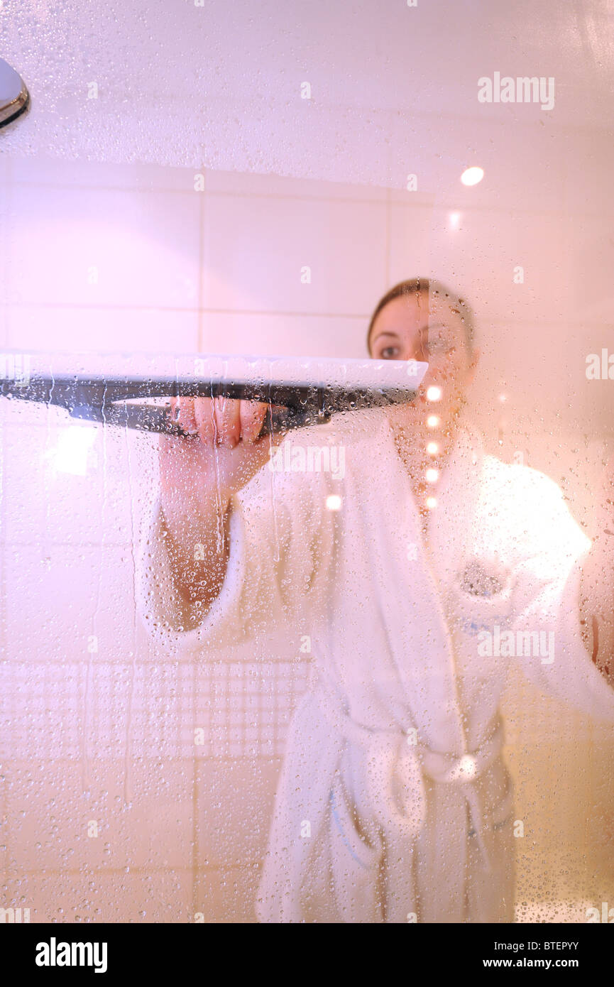 Young woman cleaning shower glass door with wiper in bathroom Stock