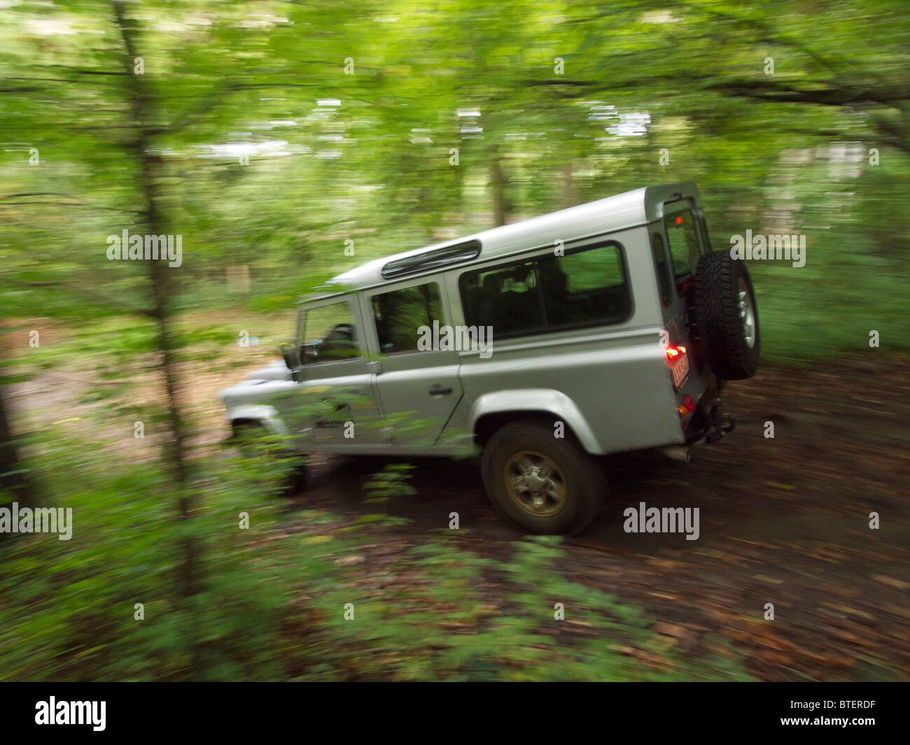 Silver Land Rover Defender driving through a forest at the Domaine d'Arthey estate in Belgium with motion blur Stock Photo