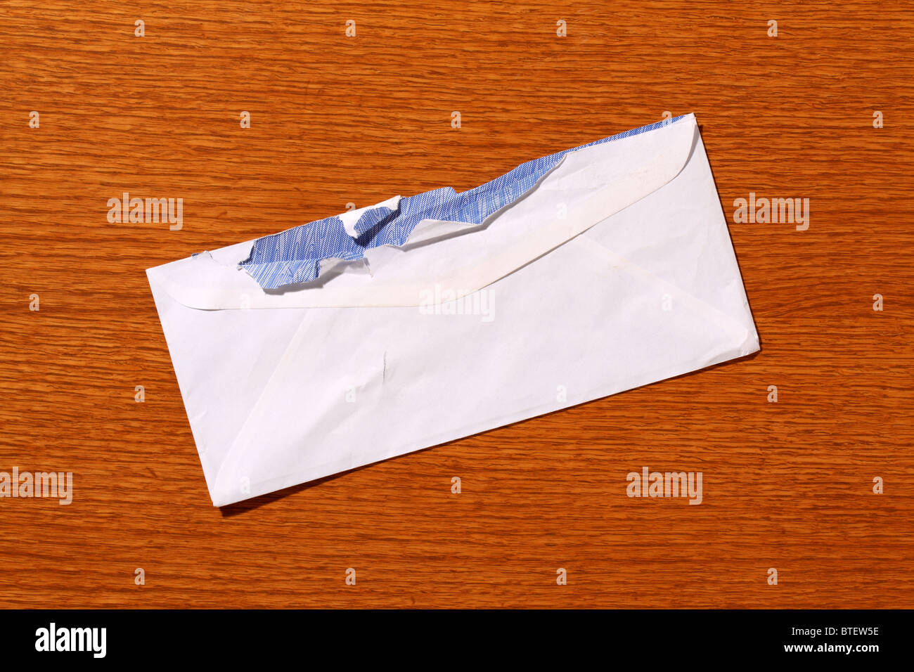 A used postal mailing envelope torn open. Brown wood grained background Stock Photo
