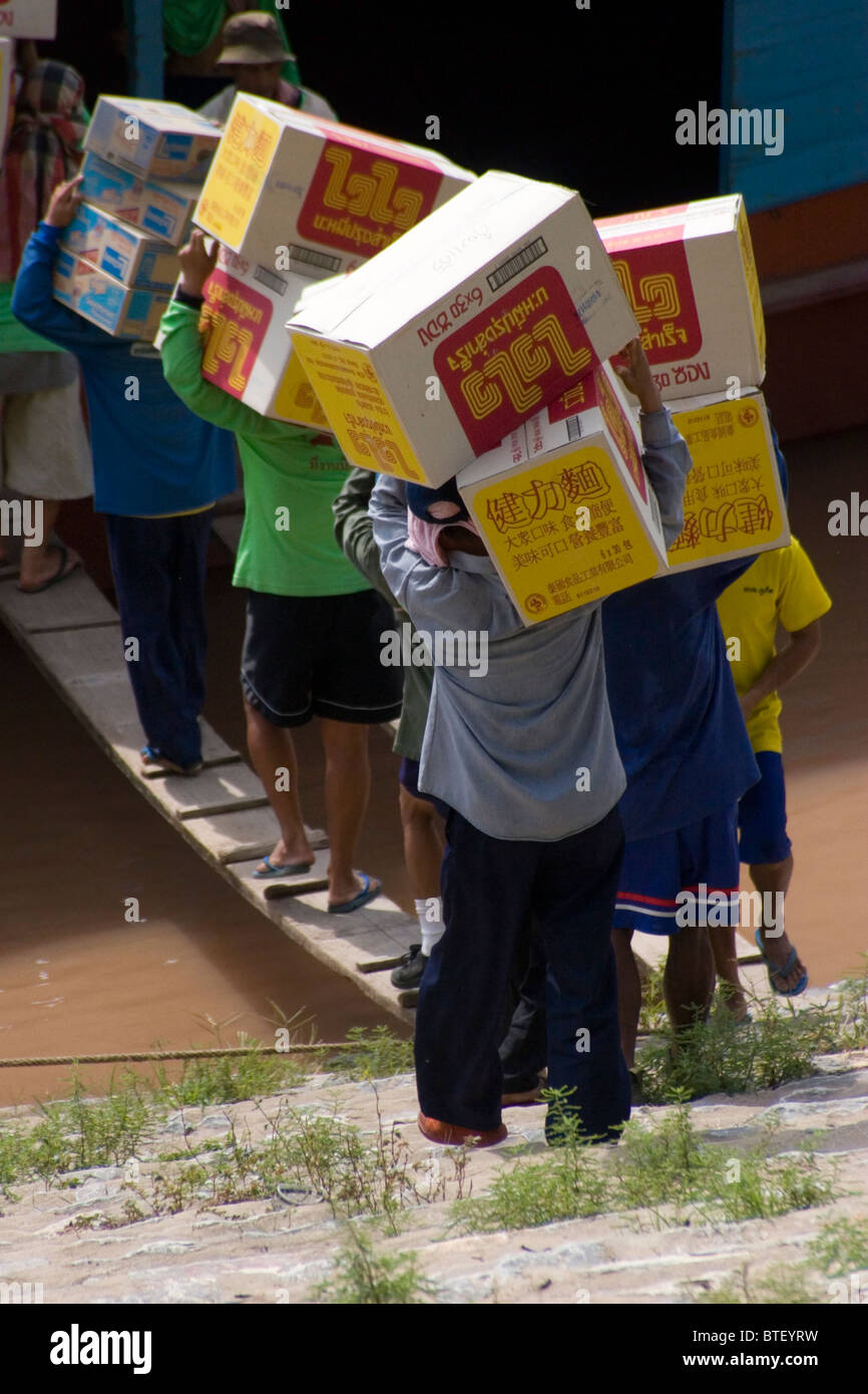 Chinese laborers are loading a cargo boat with boxes of goods on the Mekong River in Chiang Sean, Thailand. Stock Photo