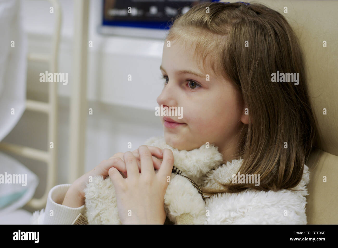 Young girl patient in a hospital ward bed cuddling a teddy bear Stock Photo