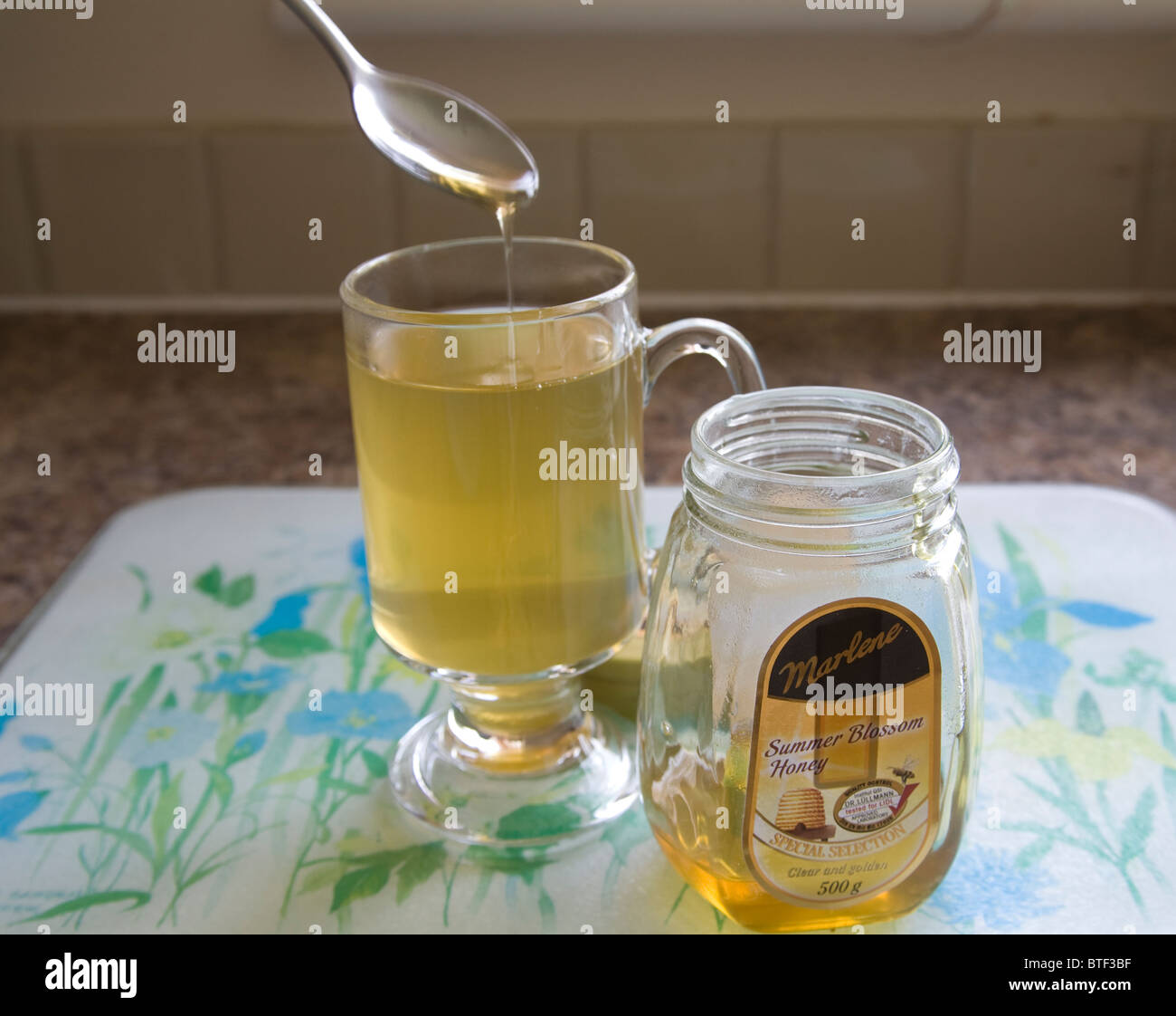 Close up spooning Summer Blossom Honey into a glass tumbler to sweeten green tea Stock Photo