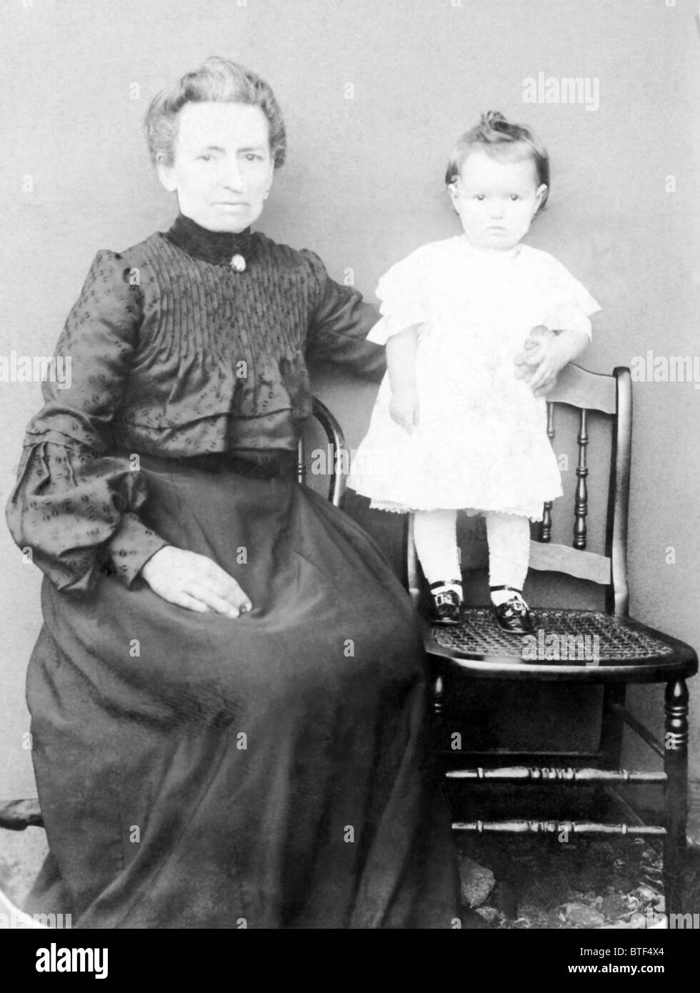 This photo taken in New Bedford, MA, in the late 1800s shows an older woman with a toddler standing on a chair. Stock Photo