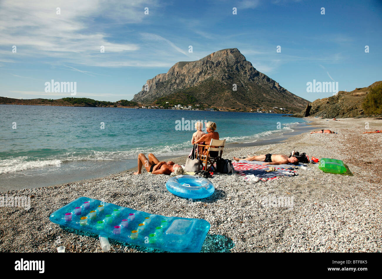 People sunbathing at Myrties beach with Telendos Island in the Front. Massouri, Kalymnos, Greece, Stock Photo