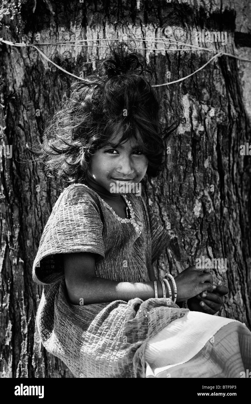 Young Indian street girl, sitting in front of a tree, smiling. Andhra Pradesh, India. Black and White Stock Photo