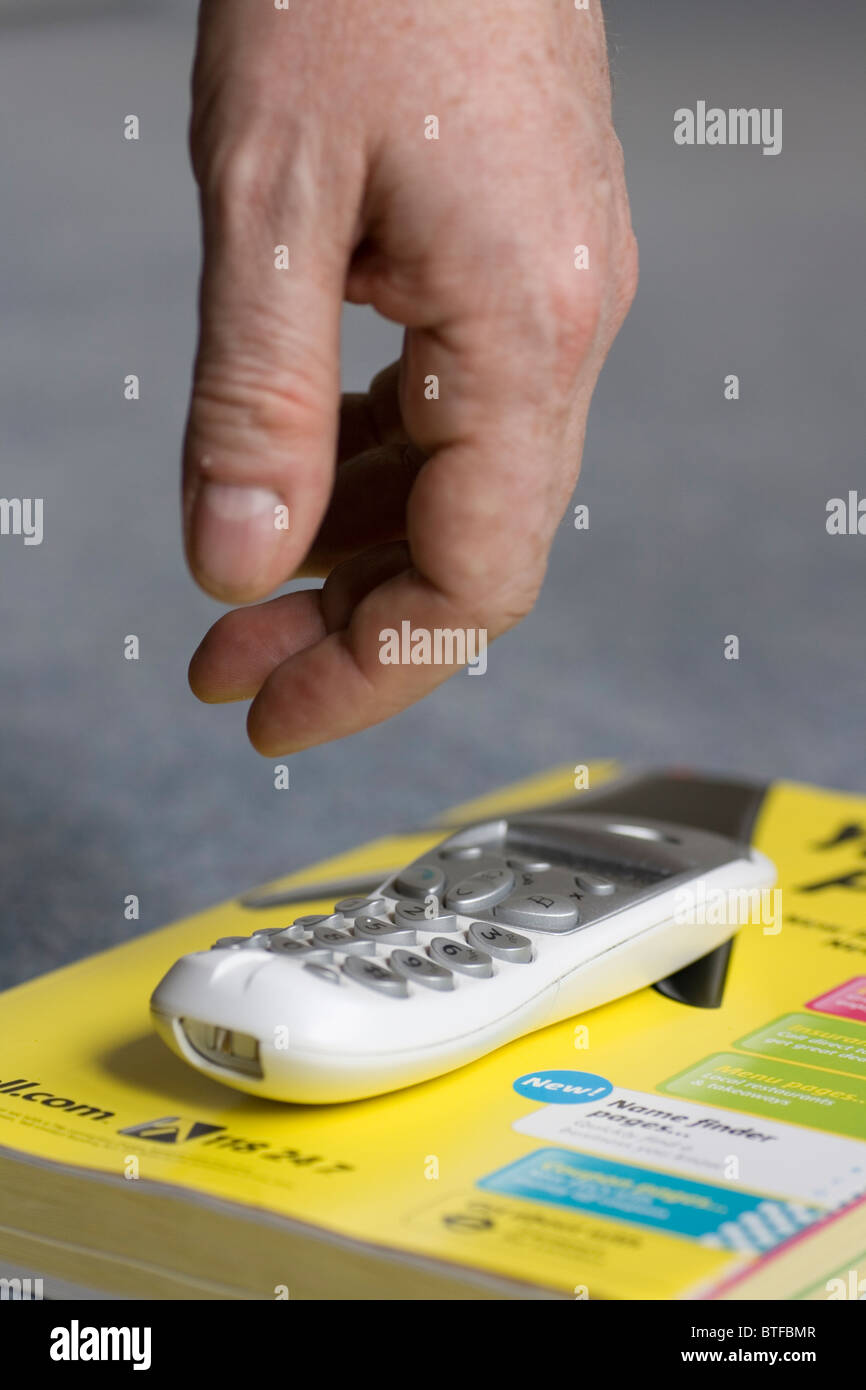 A hand reaches for a phone on a telephone directory on the floor Stock