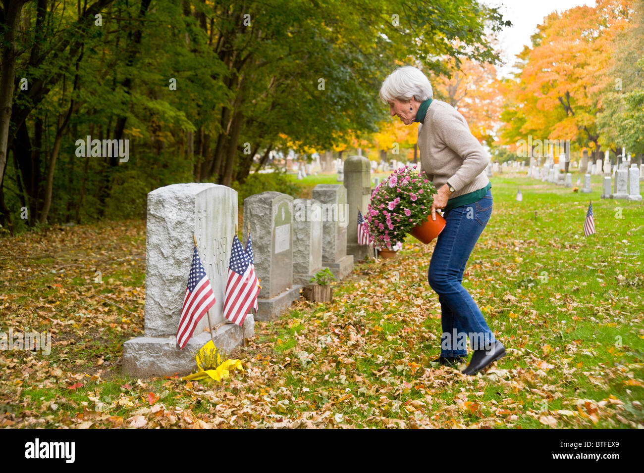 A woman places flowers on her parents' grave in a cemetery on an autumn