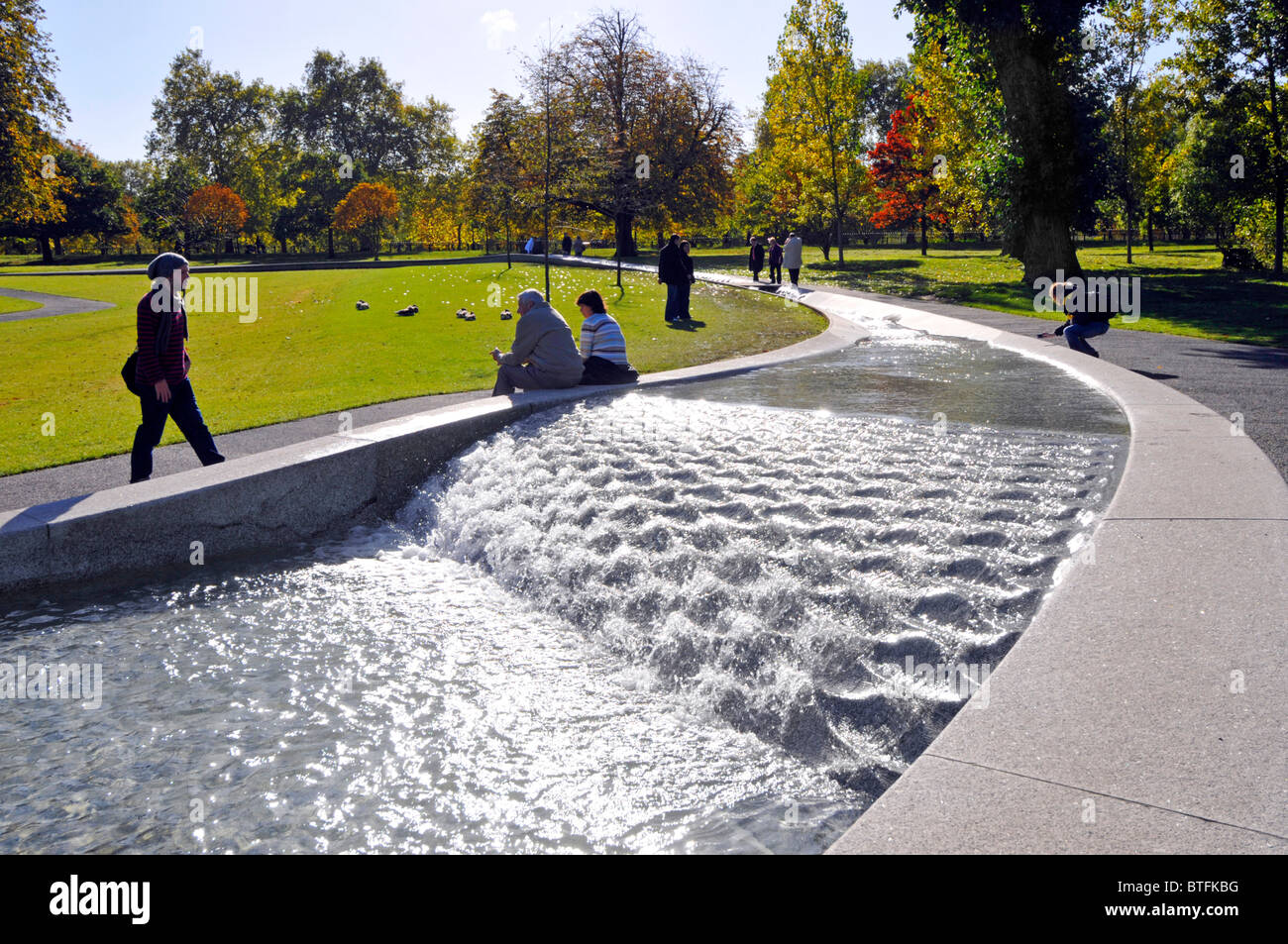 People at Princess Diana memorial fountain Hyde Park forms a circular artificial rill water feature with Autumn colours on trees London England UK Stock Photo