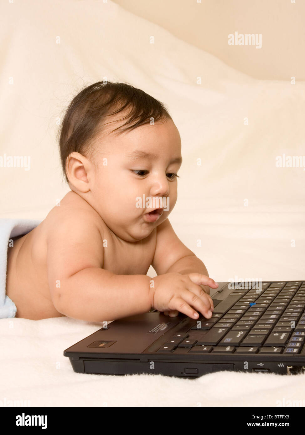 Baby playing with notebook computer keyboard, typing on it Stock Photo