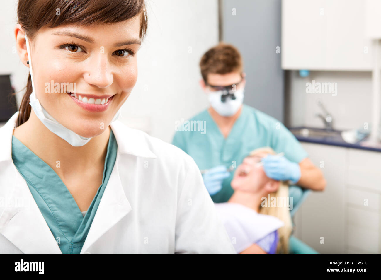 A portrait of a dental assistant smiling at the camera with the dentist working in the background Stock Photo