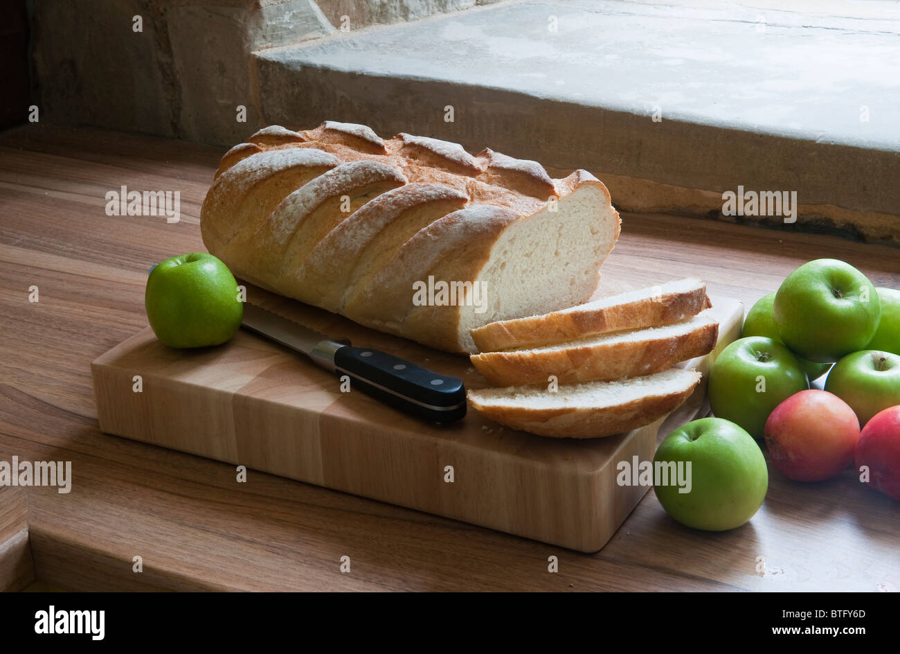 A farmhouse loaf of bread on a breadboard, with apples, UK Stock Photo